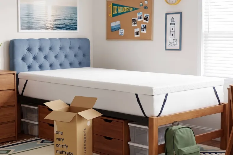 young man moving into collage putting mattress topper on his bed